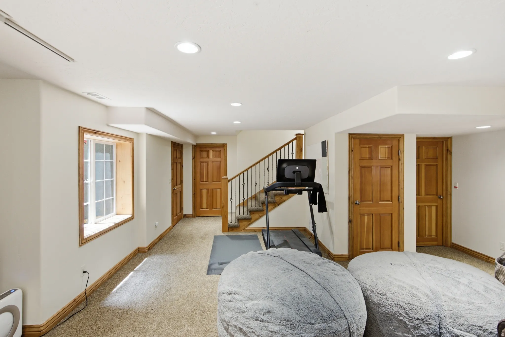 Finished lower level featuring recessed lighting, a staircase with wrought iron balusters, light wood-finish doors, and a window with wood trim