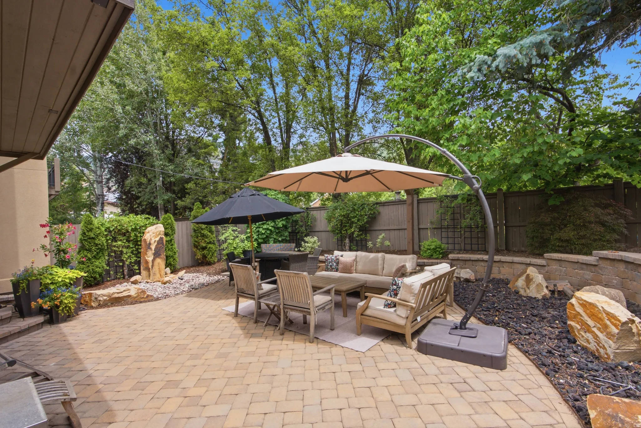 Expansive paver patio featuring a built-in stone retaining wall, decorative rock landscaping, and a stone water feature