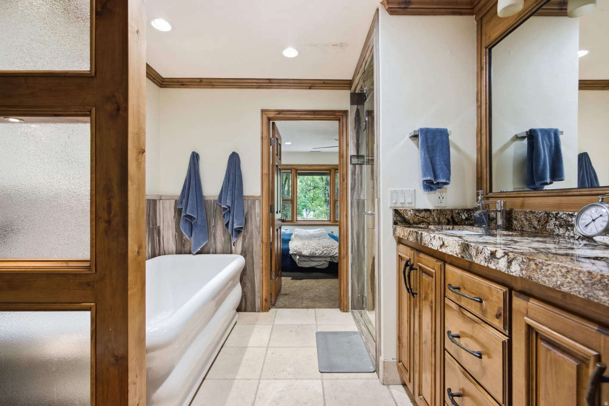 Bathroom featuring a freestanding soaking tub, wood-finish vanity with a stone countertop, a glass-enclosed shower, wood-finish trim and paneling, and ceramic tile flooring