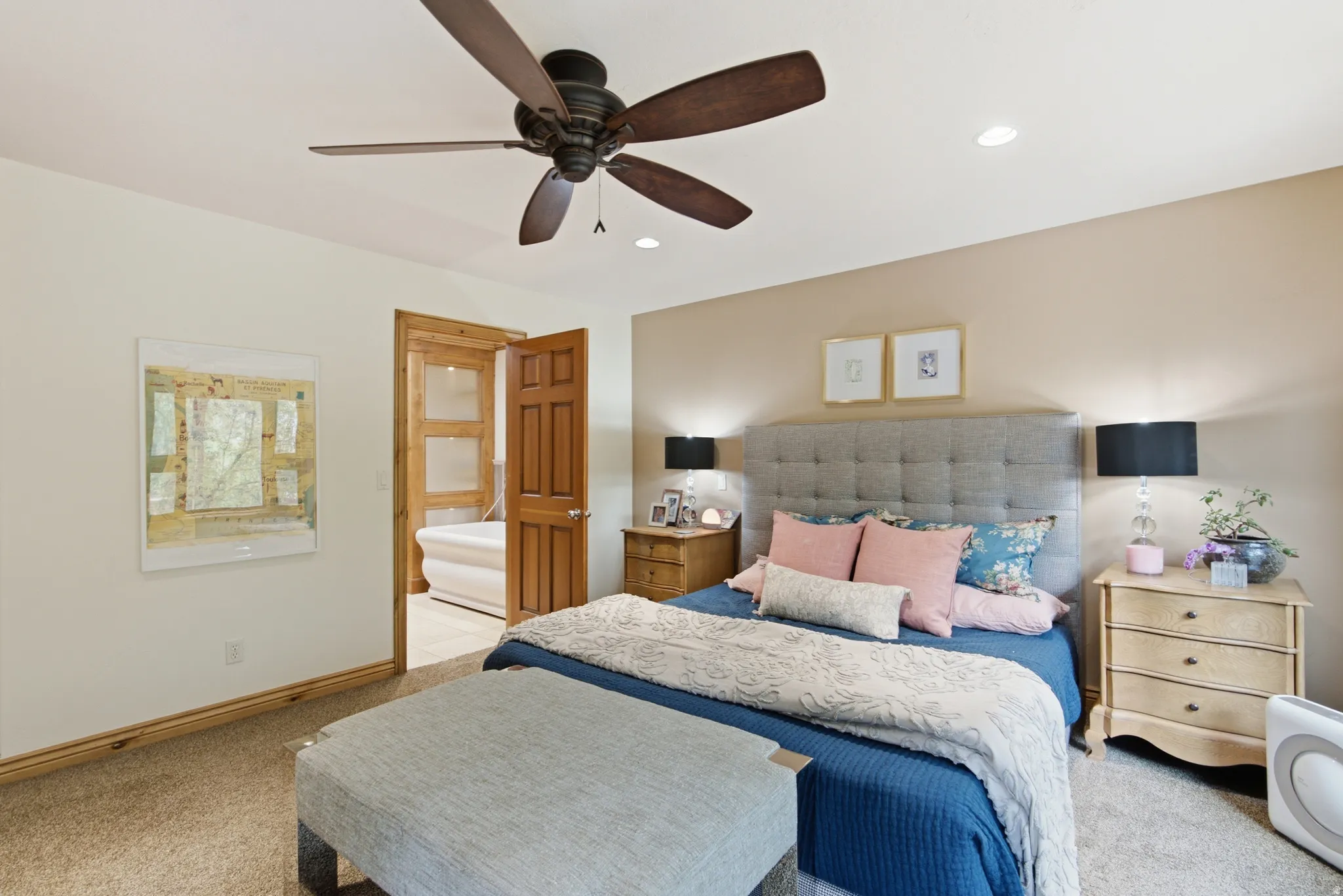 Carpeted bedroom featuring a ceiling fan with recessed lighting, wood-trim baseboards, and a wood-paneled door opening to a bathroom with a white freestanding tub