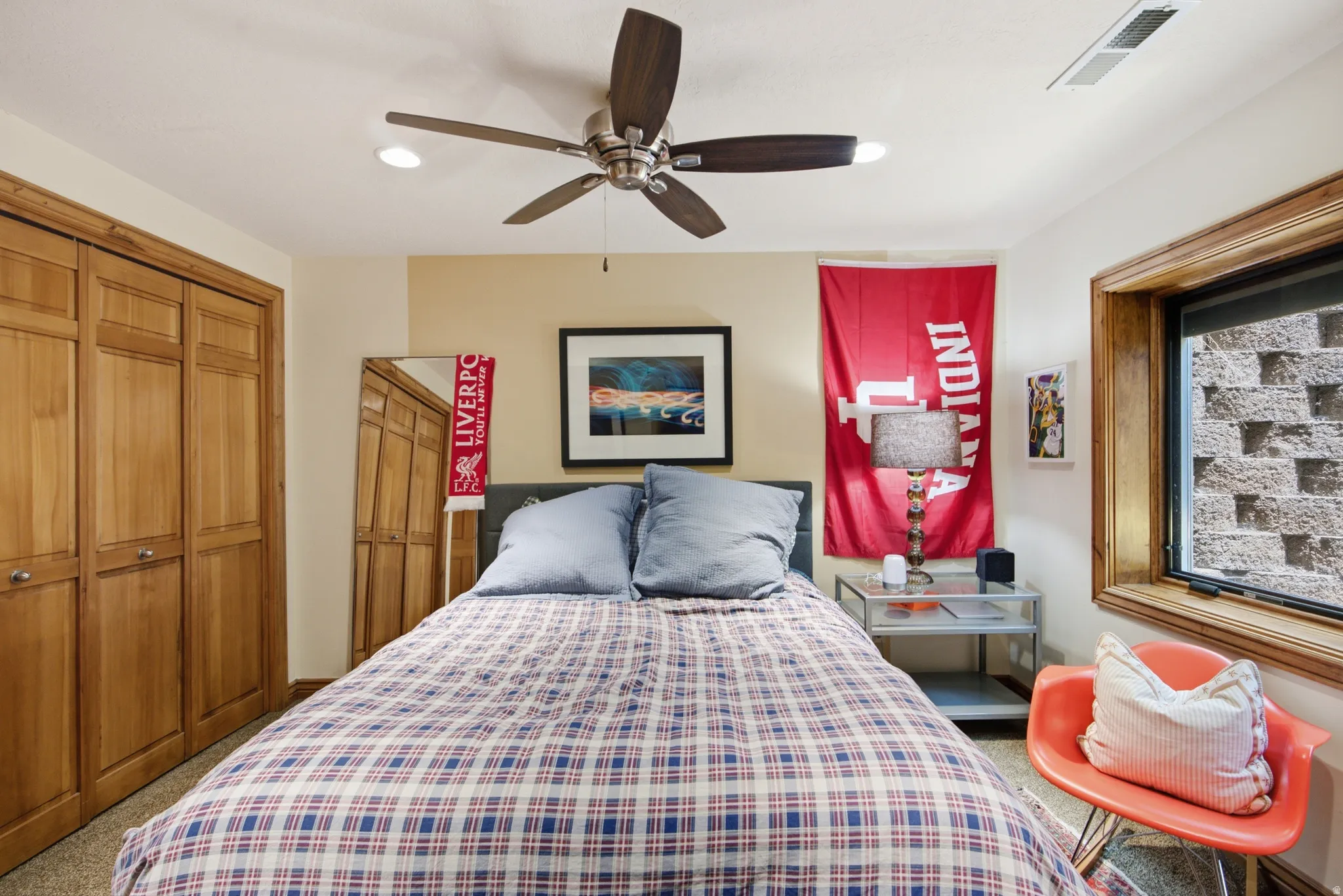 Recessed lighting illuminates this room featuring wood-finish bi-fold closet doors, a wood-trimmed window, and a ceiling fan with integrated lighting