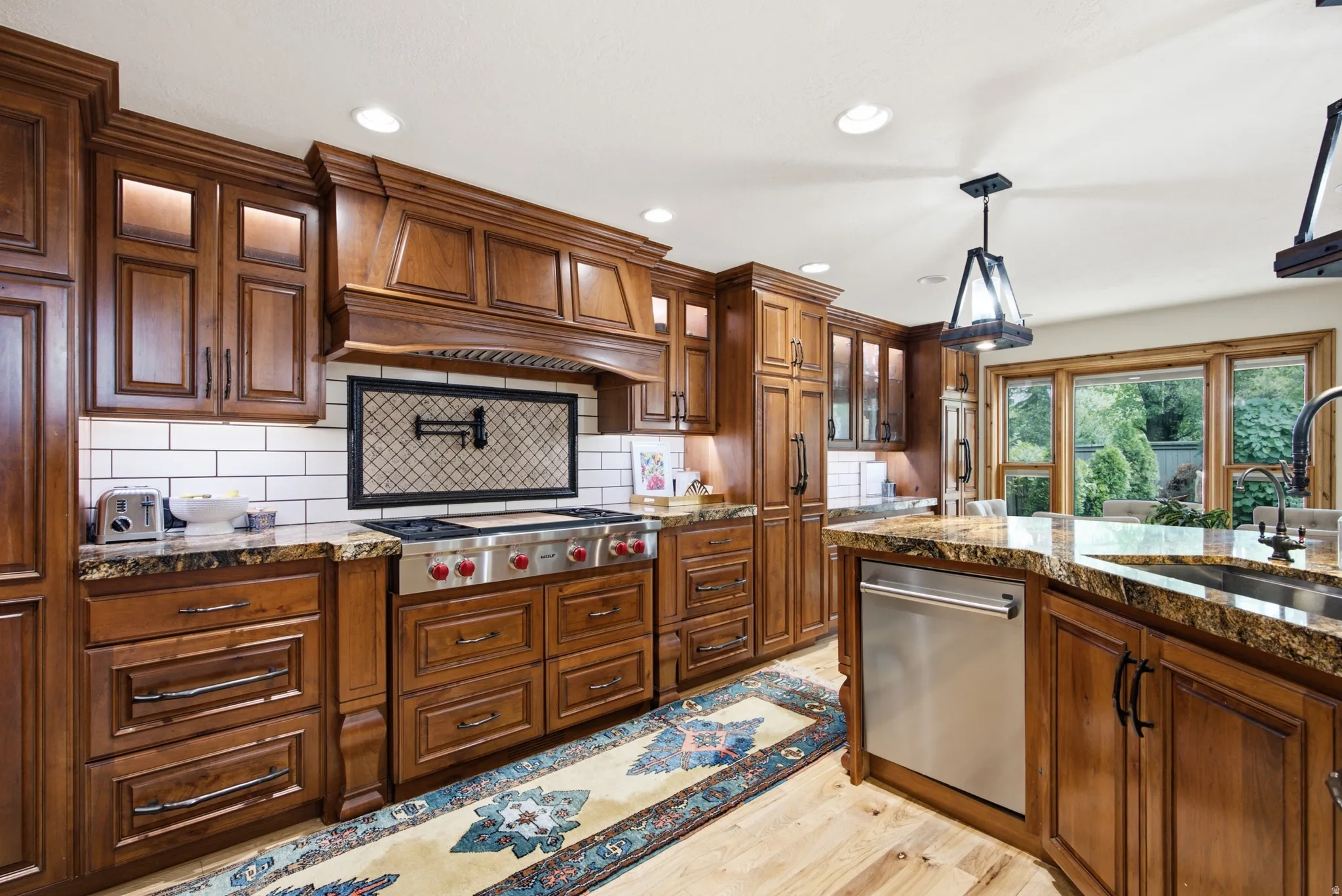 Kitchen featuring rich wood cabinetry, stone countertops, a subway tile backsplash, stainless steel appliances, and wood-finish flooring