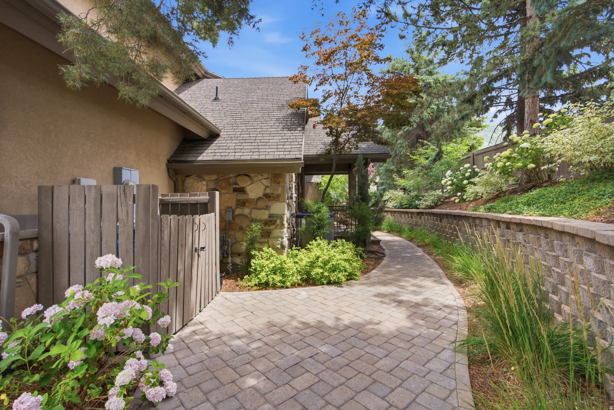 Paver pathway with a stone retaining wall, mature trees, and lush landscaping