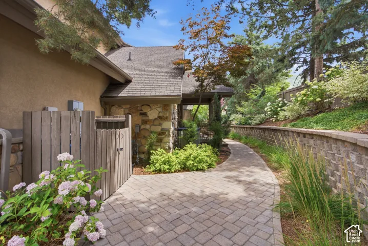 Paver pathway with a stone retaining wall, mature trees, and lush landscaping