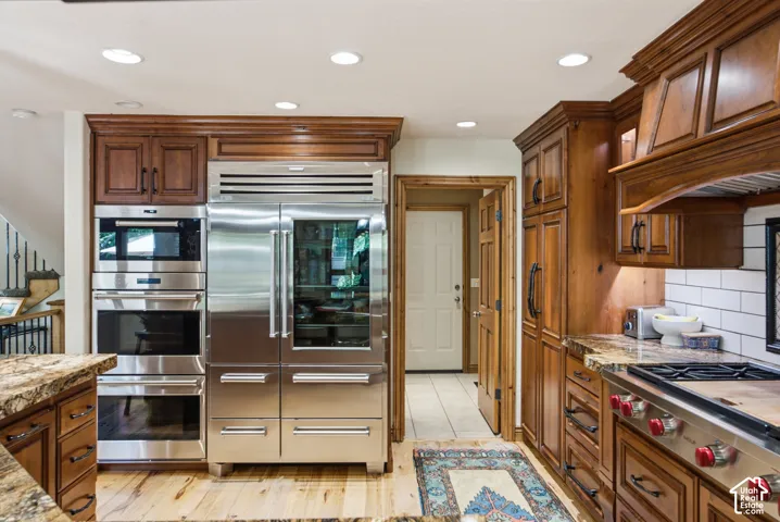 Gourmet kitchen featuring custom wood cabinetry, stainless steel appliances, a built-in double oven, paneled refrigerator, and stone countertops