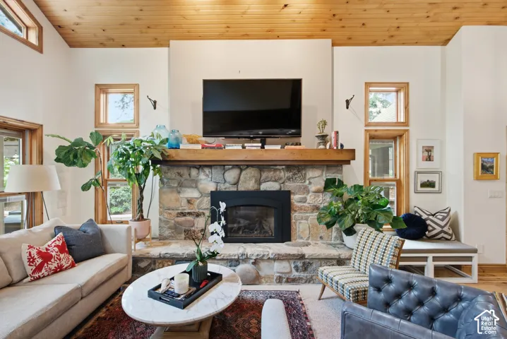 Stone-clad fireplace with a wood mantle, wood-paneled ceiling, and multiple wood-framed windows