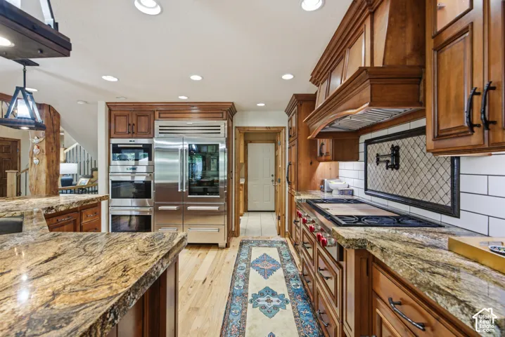Gourmet kitchen featuring granite countertops, professional-grade stainless steel appliances, custom wood cabinetry, a tiled backsplash with decorative insert, and recessed lighting