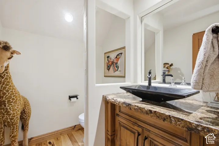 Bathroom vanity featuring a vessel sink with a black faucet, stone countertop, wood cabinetry, and a framed mirror