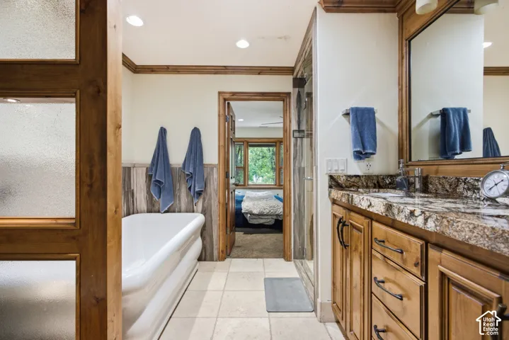 Bathroom featuring a freestanding soaking tub, wood-finish vanity with a stone countertop, a glass-enclosed shower, wood-finish trim and paneling, and ceramic tile flooring