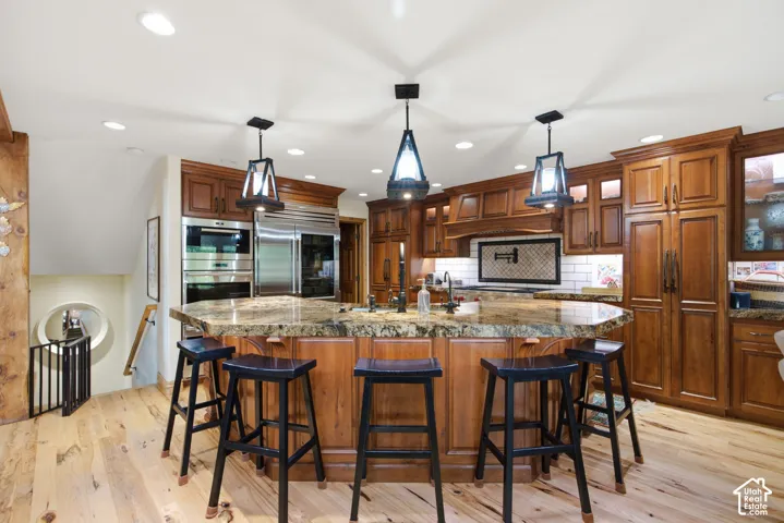 Gourmet kitchen featuring a large curved island with a stone countertop, custom wood cabinetry, stainless steel appliances, and wood-finish flooring