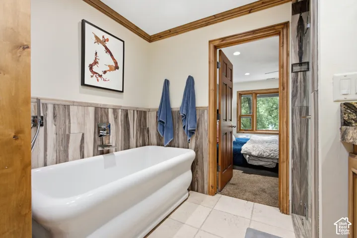 Freestanding soaking tub featuring chrome fixtures, wood-finish wainscoting, and tile flooring