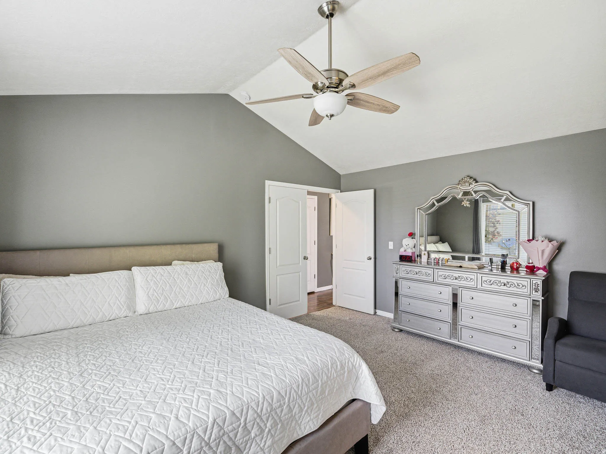 Vaulted ceiling with a ceiling fan light fixture, gray walls, light gray carpet flooring, and white interior doors