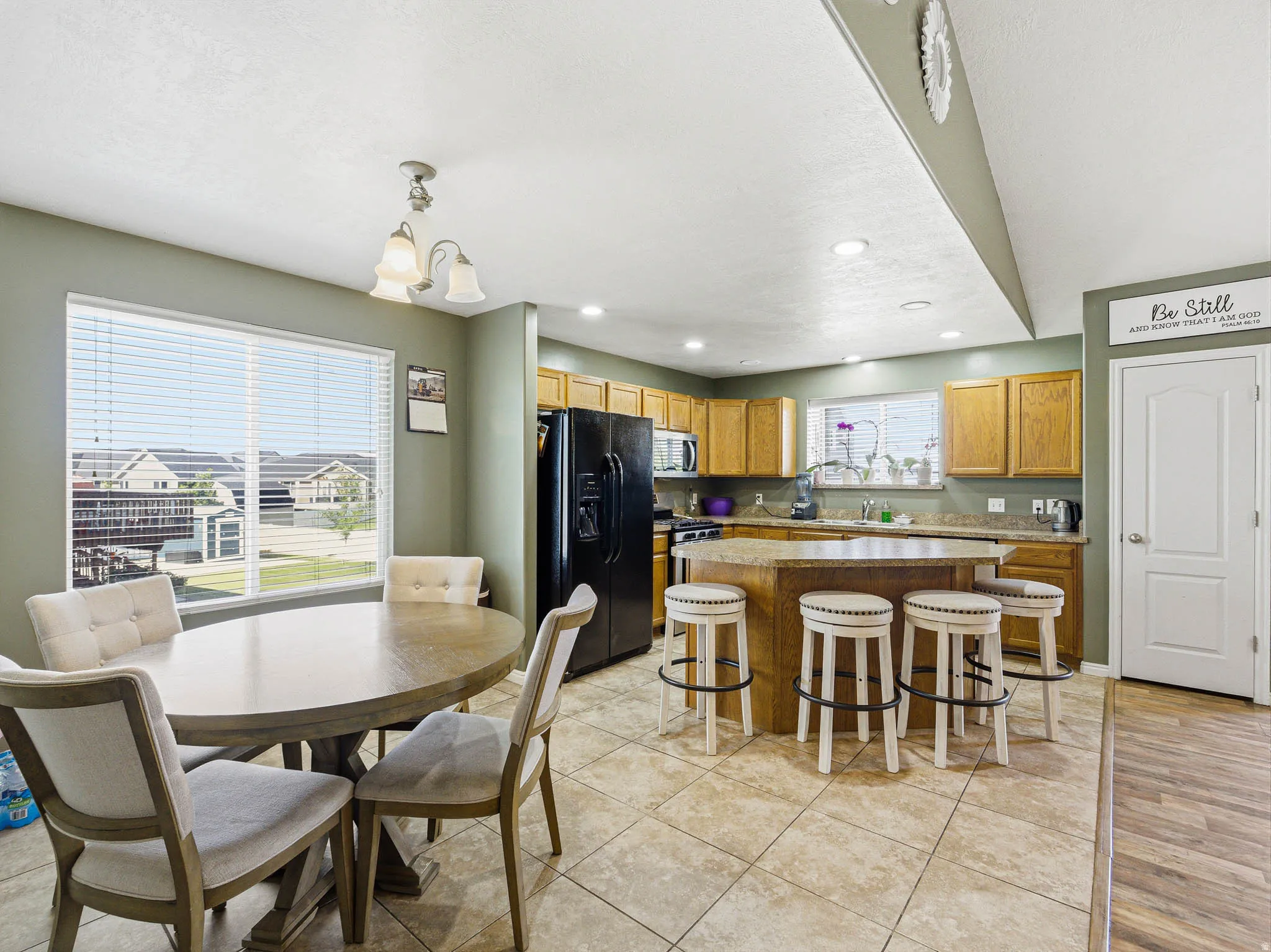 Open-concept kitchen and dining area featuring a central island with bar seating, wood-finish cabinetry, a large window, and tile flooring