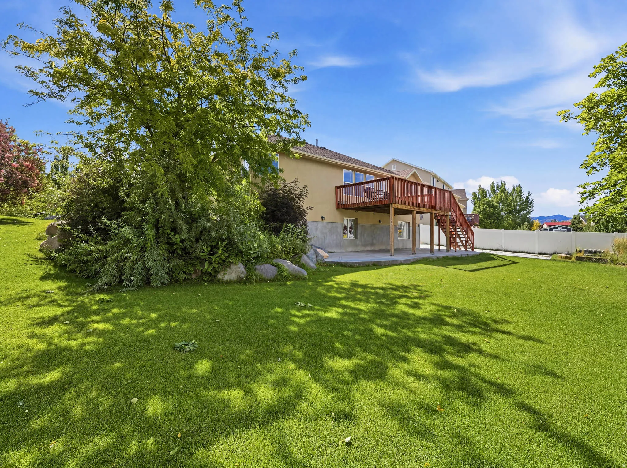 Expansive backyard featuring a lush lawn, mature trees, and a multi-level wood deck with stairs leading to a concrete patio