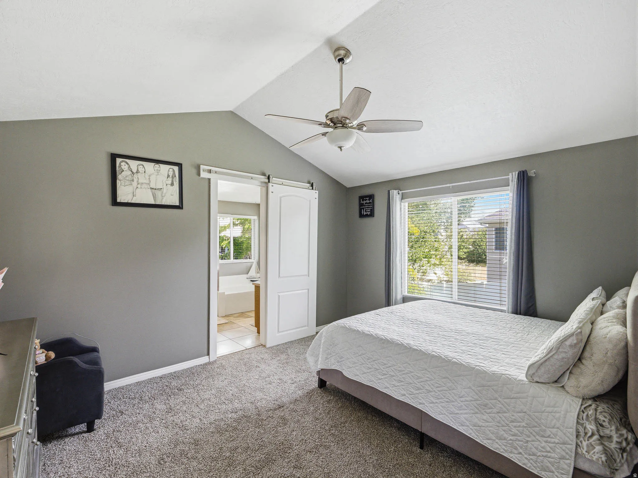 Vaulted ceiling bedroom with a ceiling fan, carpet flooring, and a large window with blinds