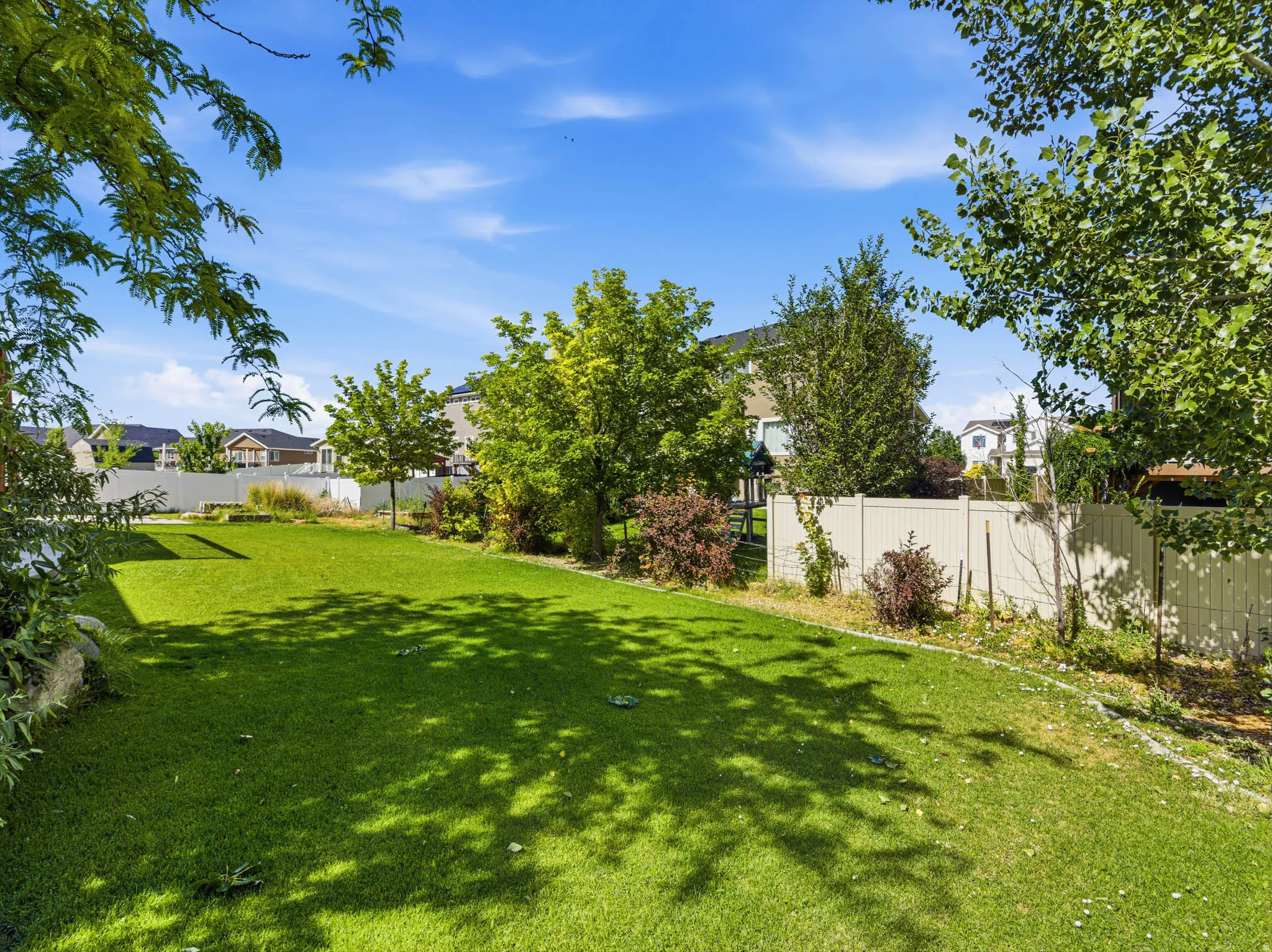 Expansive backyard featuring a lush green lawn, mature trees, and a perimeter privacy fence