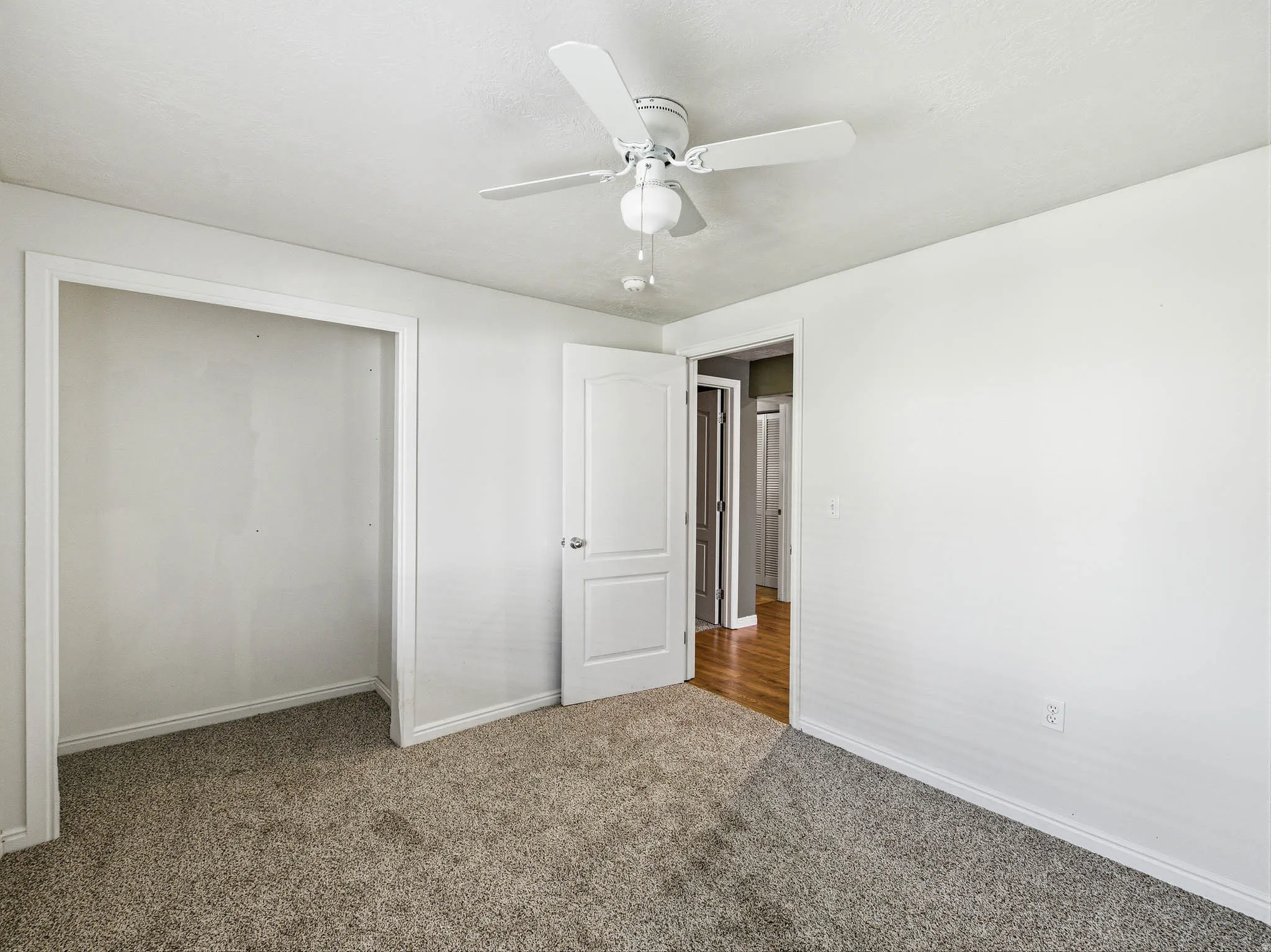 Neutral tone wall paint with matching trim, gray pile carpet, white ceiling fan, and a built-in closet space