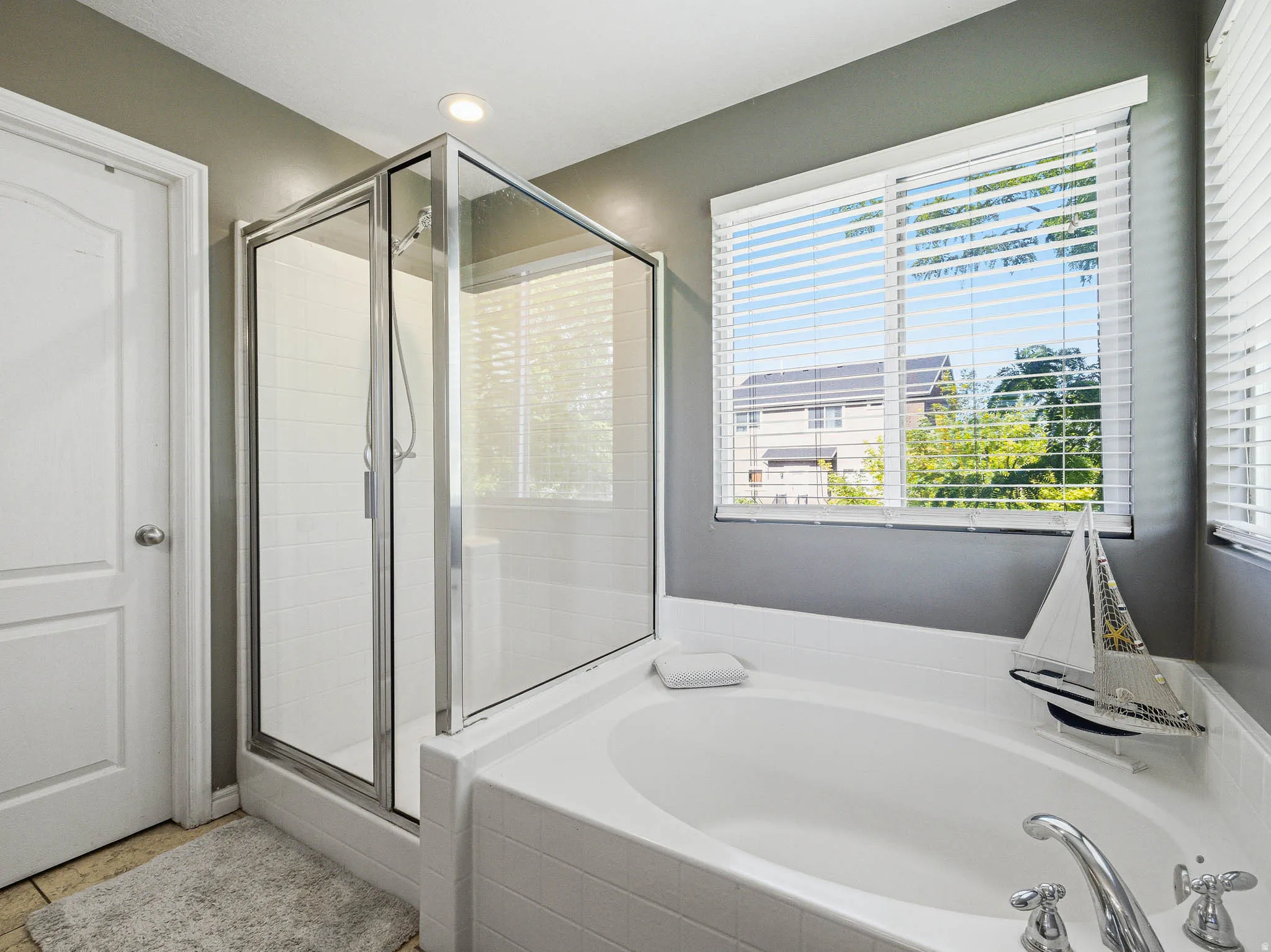 Spacious bathroom featuring a built-in soaking tub with deck-mounted fixtures, a separate glass-enclosed shower with subway tile, a window with blinds, and recessed lighting