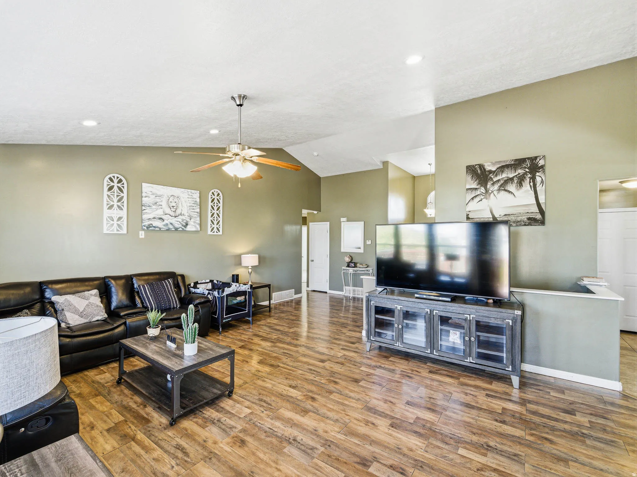 Spacious living area featuring vaulted ceilings, recessed lighting, wood-finish flooring, and a ceiling fan with integrated lighting