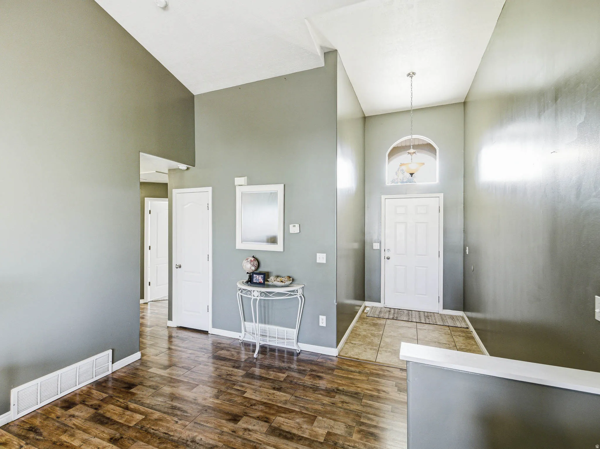 Entryway featuring vaulted ceilings, a white paneled front door with an arched transom window, and a chandelier