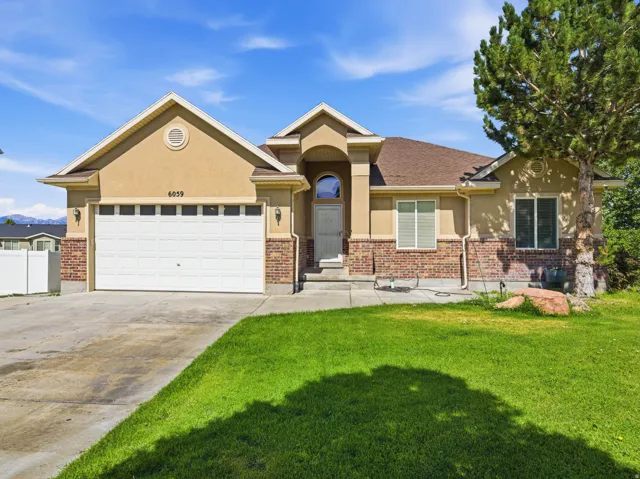 Front exterior featuring a two-car garage, brick accents, and a mature tree