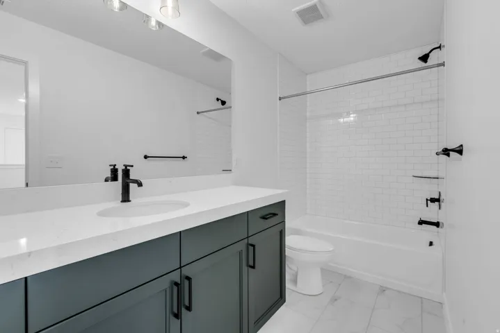 Bathroom featuring a wood painted  vanity with a white quartz countertop and custom undermount sink, a large mirror with vanity lighting, and black fixtures.