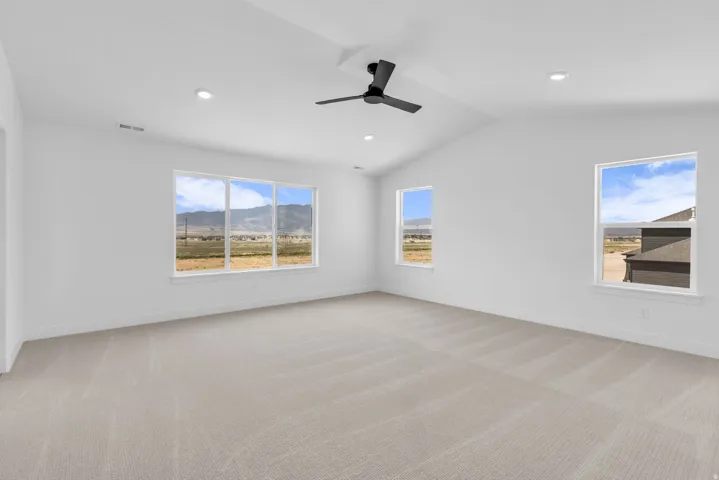 Spacious primary bedroom featuring vaulted ceilings, a contemporary ceiling fan, LED lighting, expansive windows, and light-toned carpeting.