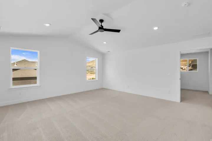 Spacious primary bedroom featuring vaulted ceilings, LED lighting, a modern black ceiling fan, and light-toned carpeting.