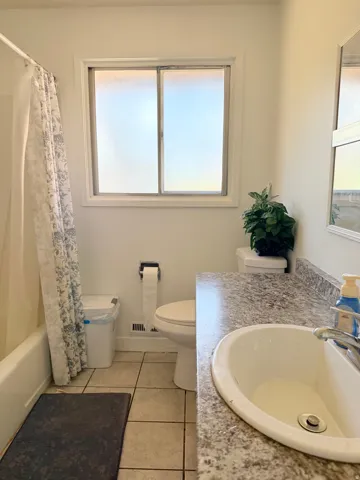 Bathroom featuring a tiled floor, white bathtub with shower, white toilet, and a vanity with a laminate countertop and integrated sink