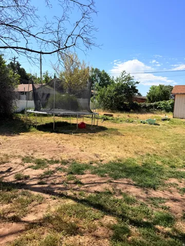 Expansive outdoor space featuring a detached storage shed with a shingled roof, mature perimeter foliage, and partial fencing