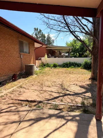 Spacious backyard with a covered patio, brick exterior, and mature trees