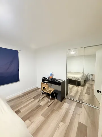 Room featuring wood-finish flooring, white walls, and a window with a blue roller shade