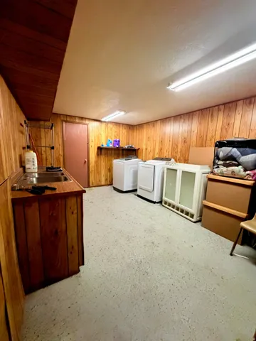 Utility room featuring wood paneling, a built-in sink with cabinetry, and concrete flooring