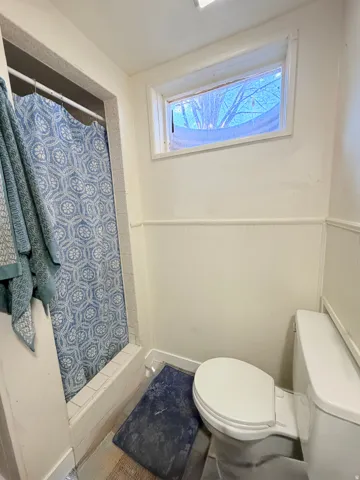 Bathroom featuring a white toilet, wainscoting, and a window with trim