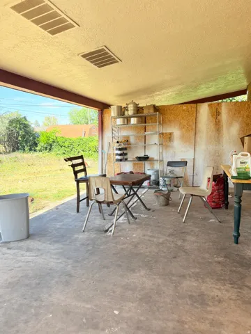 Covered patio space featuring a concrete floor, exposed structural beams, and a textured ceiling with two recessed vents