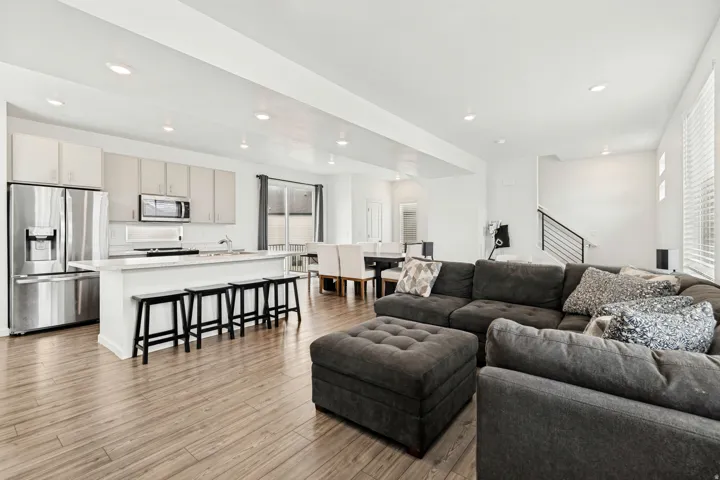 Open-concept living area featuring wood-finish flooring, a kitchen island with seating, stainless steel appliances, white cabinetry, and recessed lighting