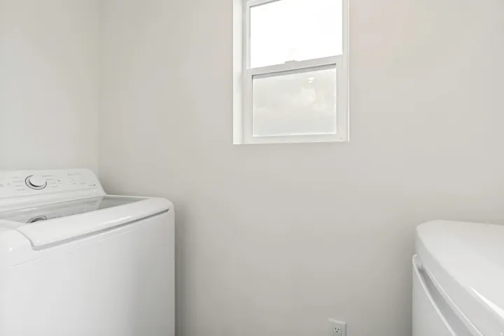 Dedicated laundry area with light gray walls, a white framed window, and a white electrical outlet