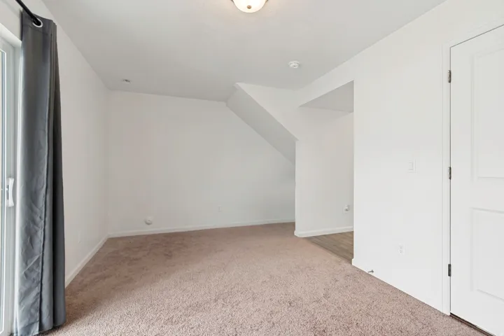 Carpeted living area with white walls and baseboards, featuring a sliding glass door with a dark curtain