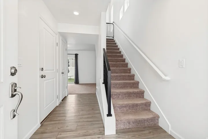 Entryway featuring wood-finish flooring and a carpeted staircase with a black metal railing