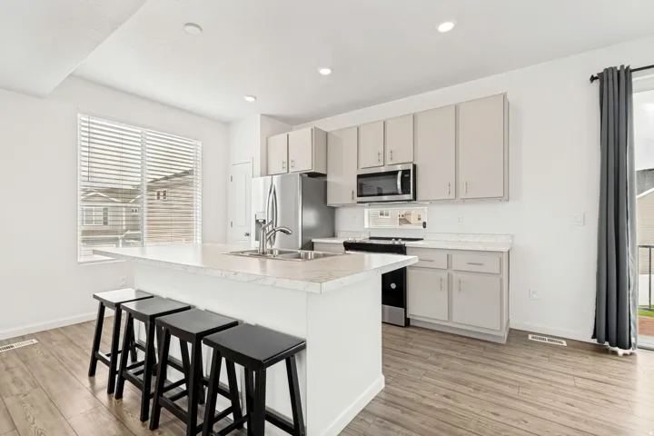 Modern kitchen featuring a large island with seating, stainless steel appliances, light-toned cabinetry, and wood-finish flooring