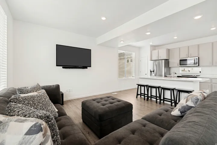 Open-concept living space featuring wood-finish flooring, recessed lighting, and a kitchen with light cabinetry, stainless steel appliances, and a breakfast bar
