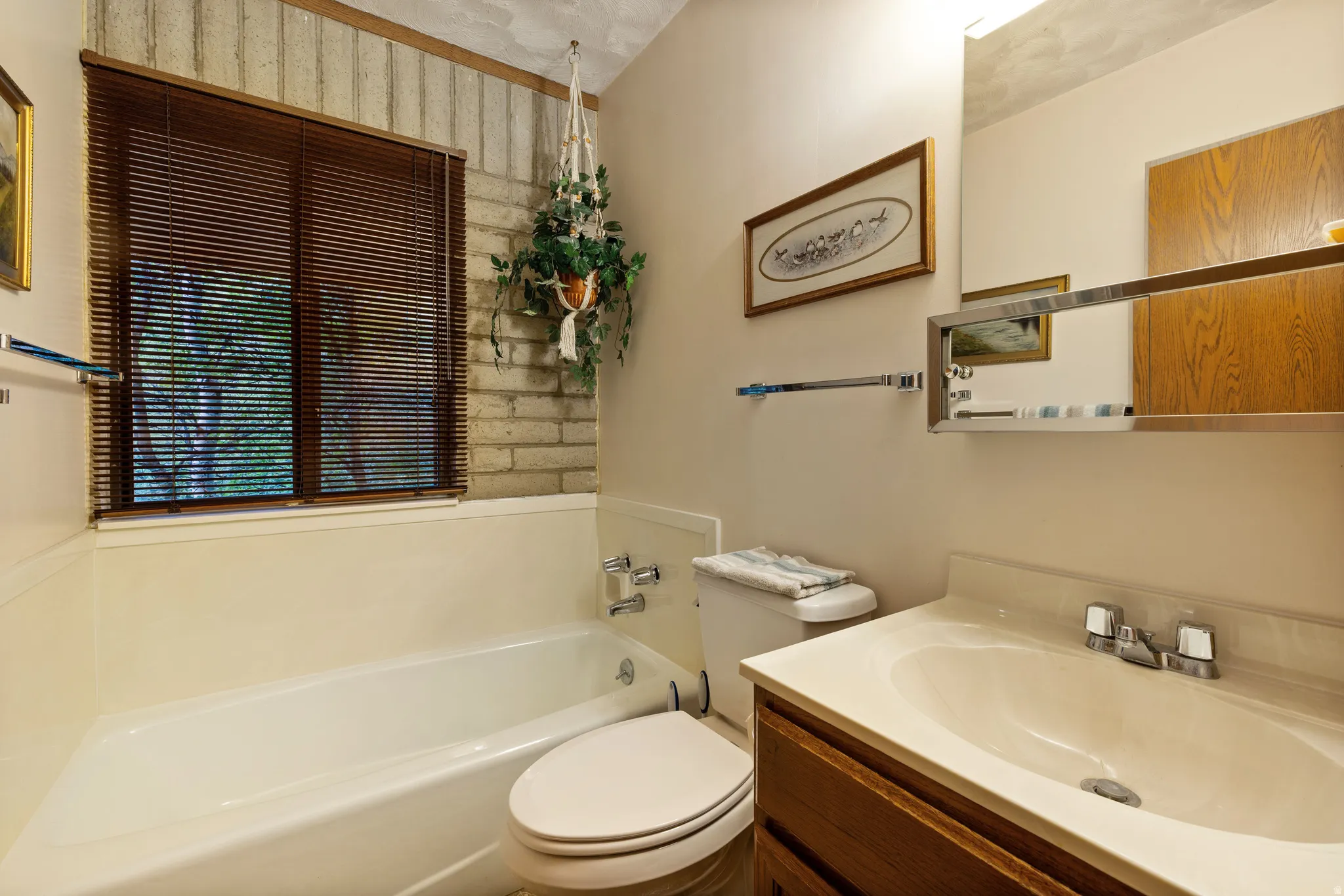 Bathroom featuring a window with wood-finish blinds, a built-in tub, and a vanity with an integrated sink and wood-finish cabinetry