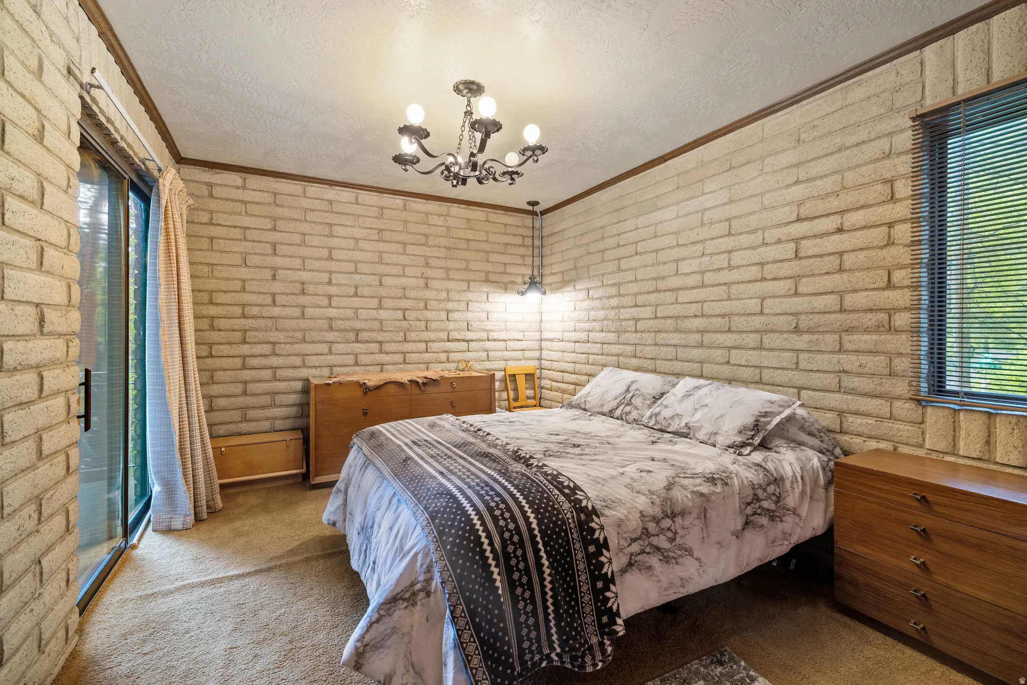 Bedroom featuring brick walls frame this room, featuring a sliding glass door with vertical blinds and an overhead chandelier light fixture