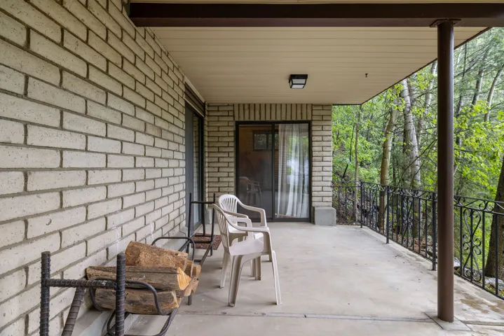 Covered patio featuring a concrete surface, light brick exterior, dark metal railing, and a sliding glass door