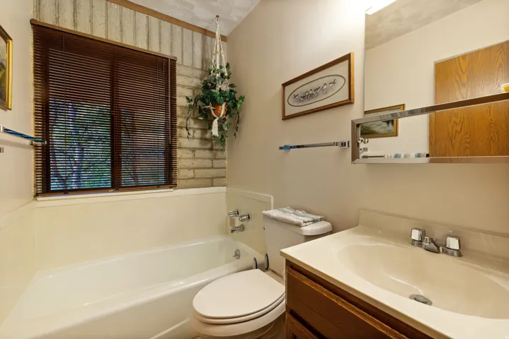 Bathroom featuring a window with wood-finish blinds, a built-in tub, and a vanity with an integrated sink and wood-finish cabinetry
