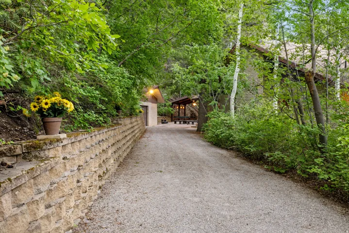 Gravel driveway bordered by a retaining wall and lush, mature trees