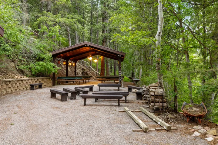 Gravel patio with a covered outdoor structure featuring pendant lighting, integrated seating, and surrounding mature trees