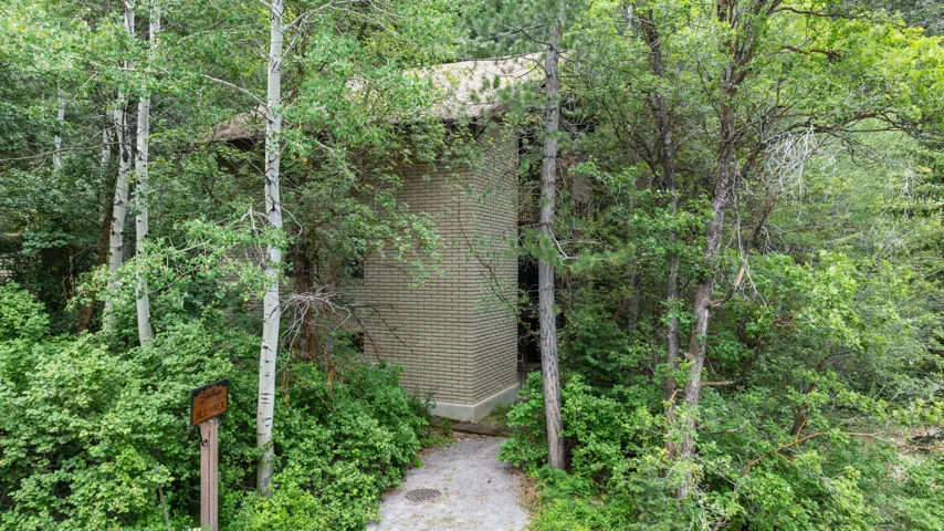 Brick exterior cabin surrounded by mature deciduous trees and lush vegetation