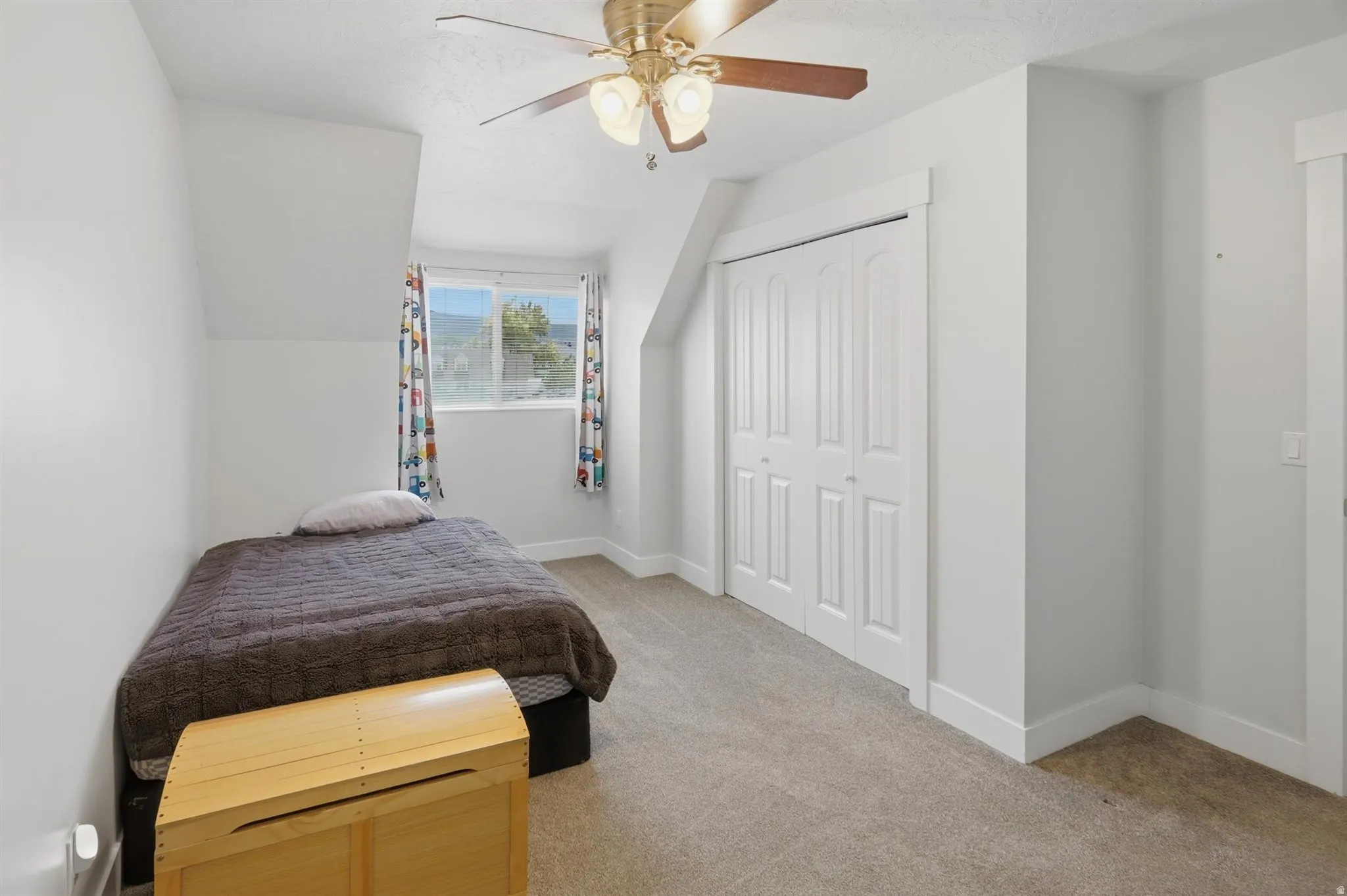 Carpeted room featuring a ceiling fan with light fixture, white walls, and a window with a mountain backdrop