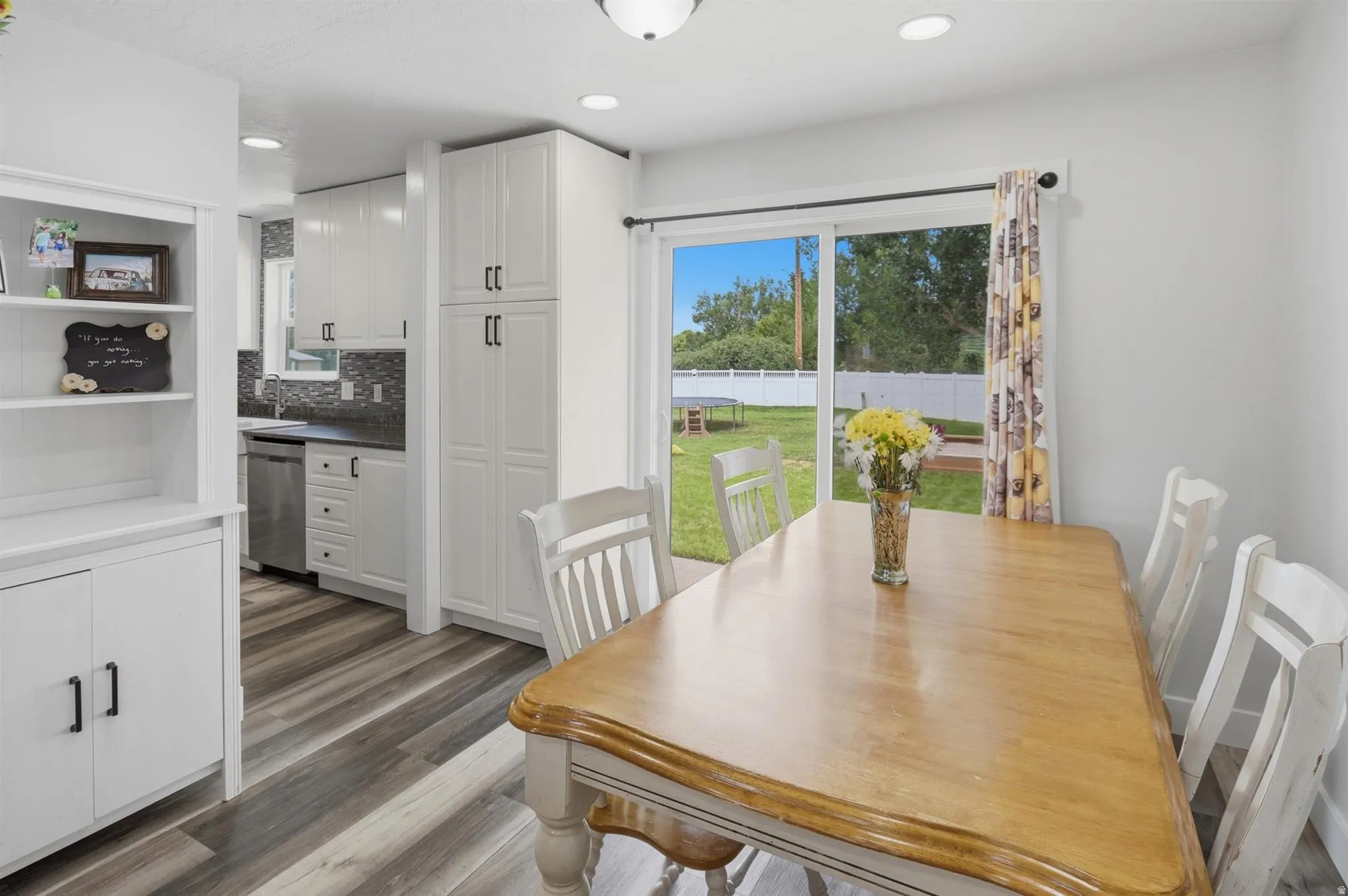 Open-concept dining area featuring wood-finish flooring, a sliding glass door to the backyard, recessed lighting, white built-in cabinetry, and a kitchen with stainless steel appliances and a dark tile backsplash